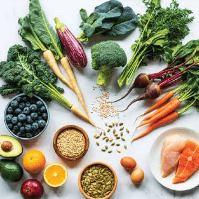 Whole foods arranged on a table: greens, roots, grains, eggs, and fish